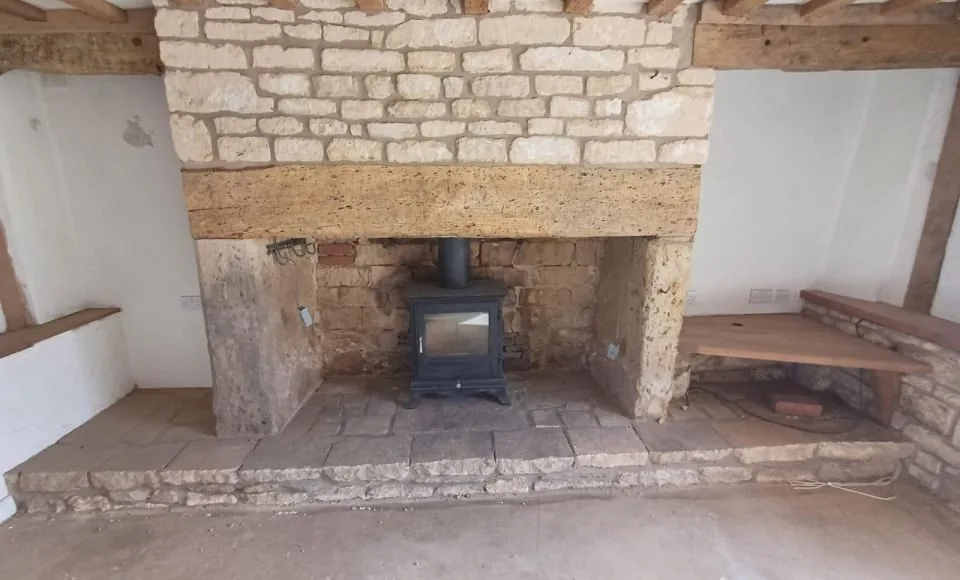 Detailed restored stone fireplace beneath bright natural oak ceiling beams