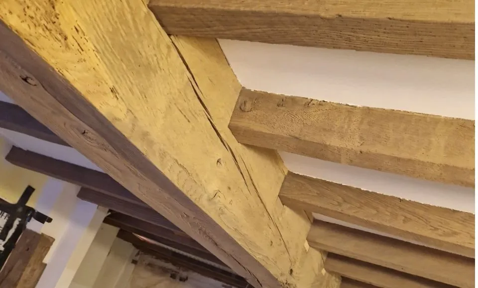 Lightened oak ceiling beams after controlled cleaning, with a clearer natural grain and a softer, more even timber tone.
