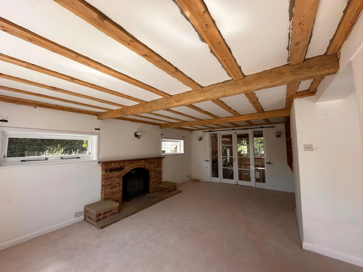 Warm natural timber ceiling beams restored above a bright cottage room and traditional brick fireplace after cleaning