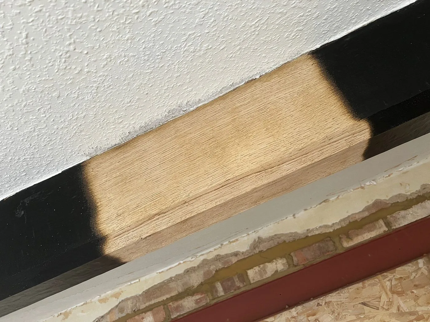 Restored central section of an oak ceiling beam with warm grain beside remaining dark paint