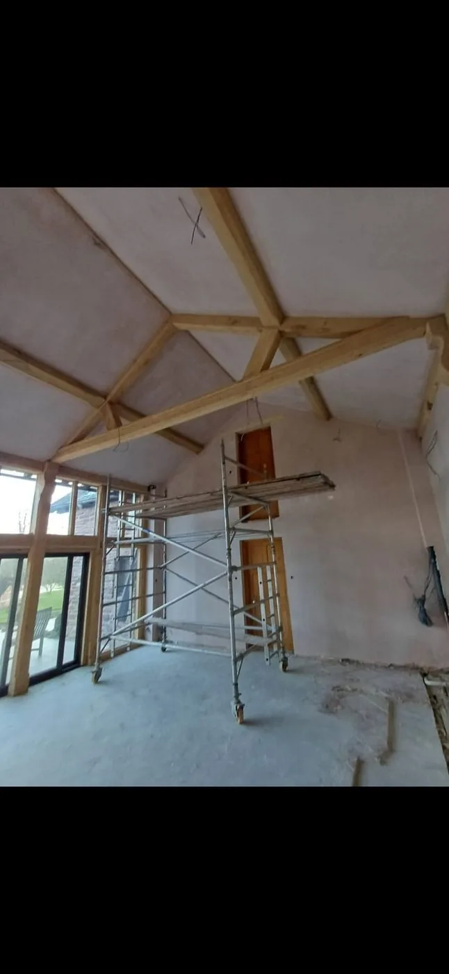 Clean honey-toned oak beams and trusses with restored grain beneath a vaulted plaster ceiling