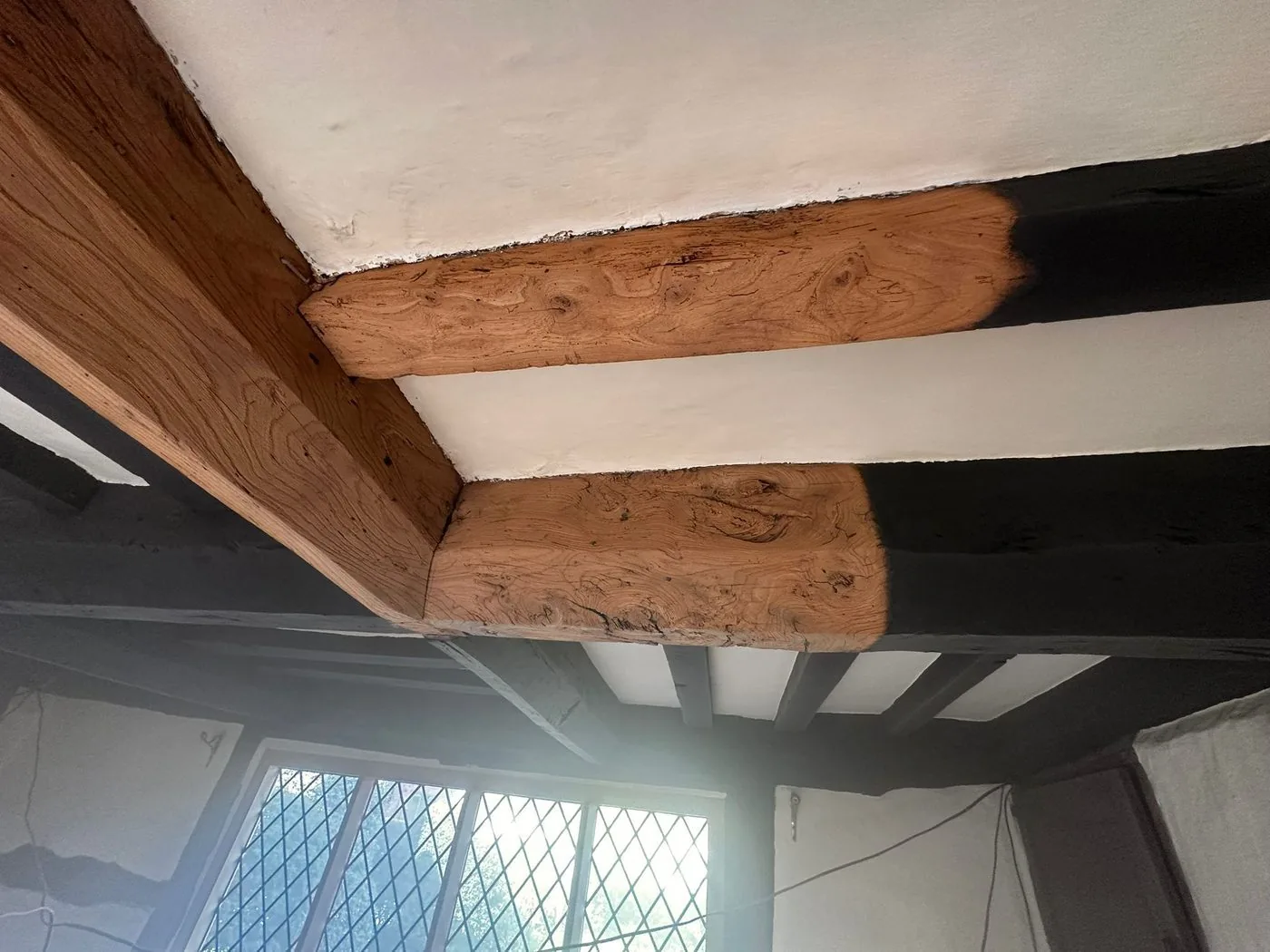 Later restoration stage on the cottage oak beams, with cleaned timber detail emerging as the heavy finish is reduced.