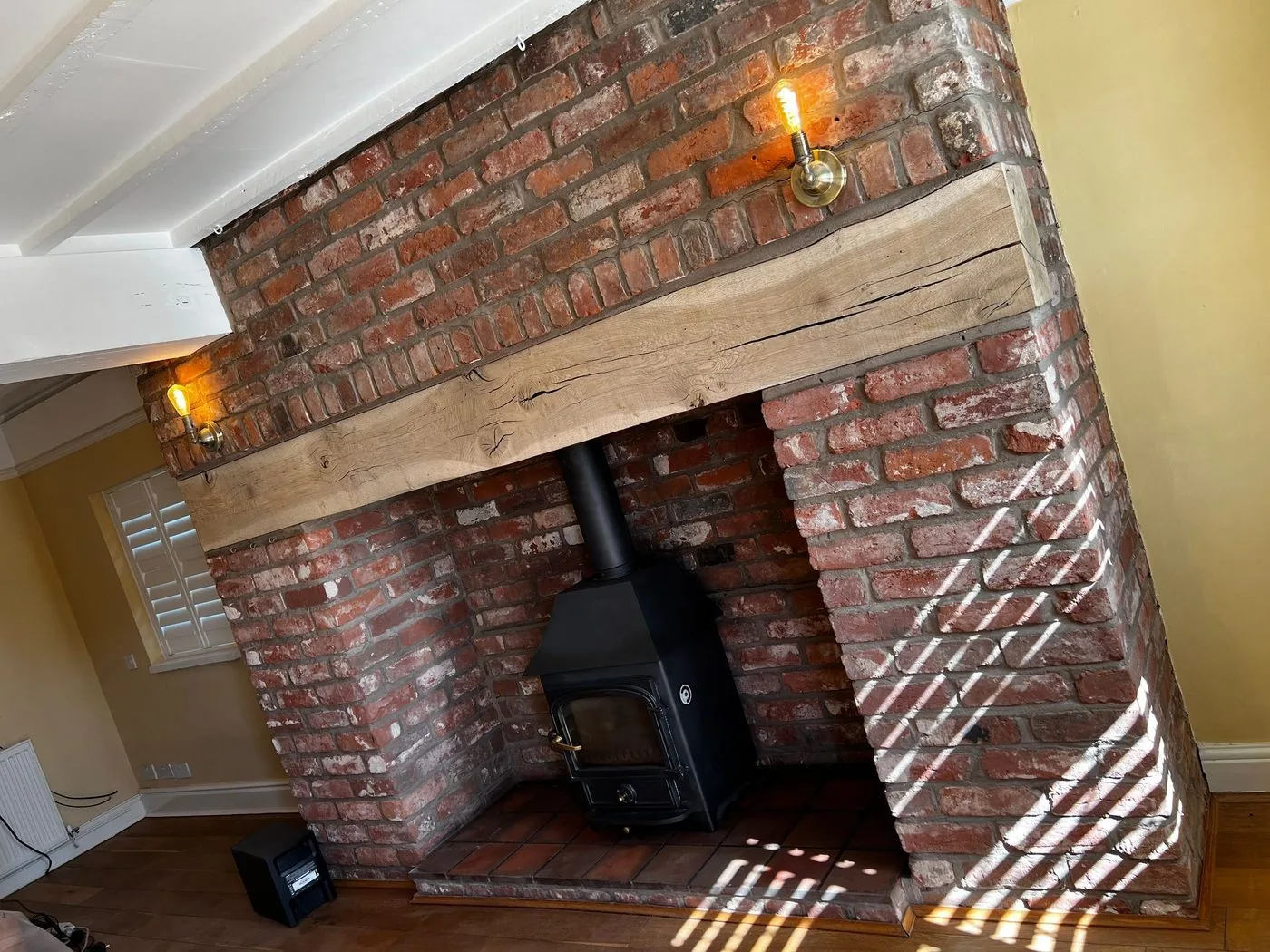 Restored oak mantel beam with visible natural grain framing the clean brick inglenook and stove