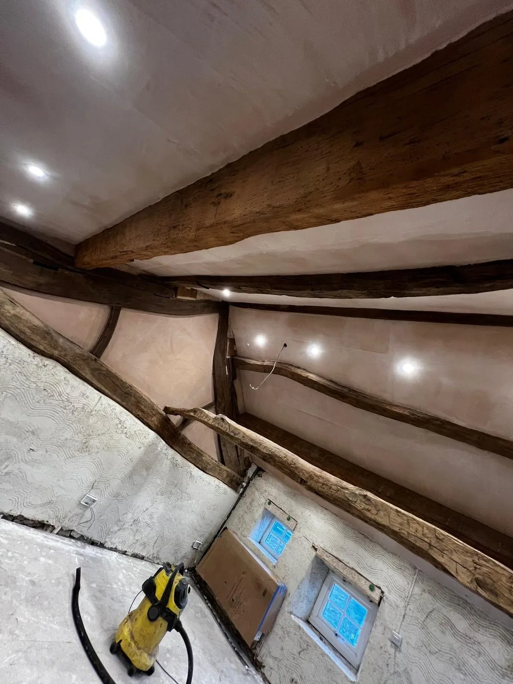Clean oak ceiling beams and bright stone fireplace showing restored texture and detail