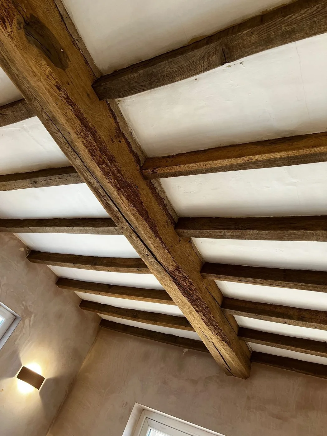 Restored oak ceiling beams showing natural grain beside traditional lime plaster infill