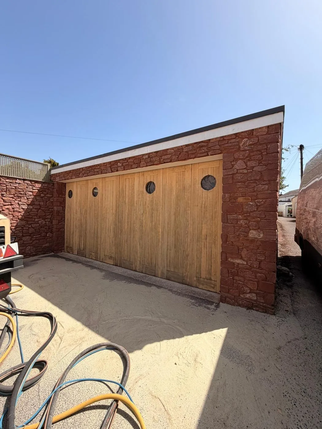 Restored pale oak garage doors with clean circular porthole details framed by red sandstone
