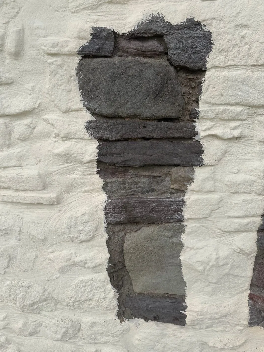 Stone farmhouse exterior during controlled white paint removal showing restored stonework