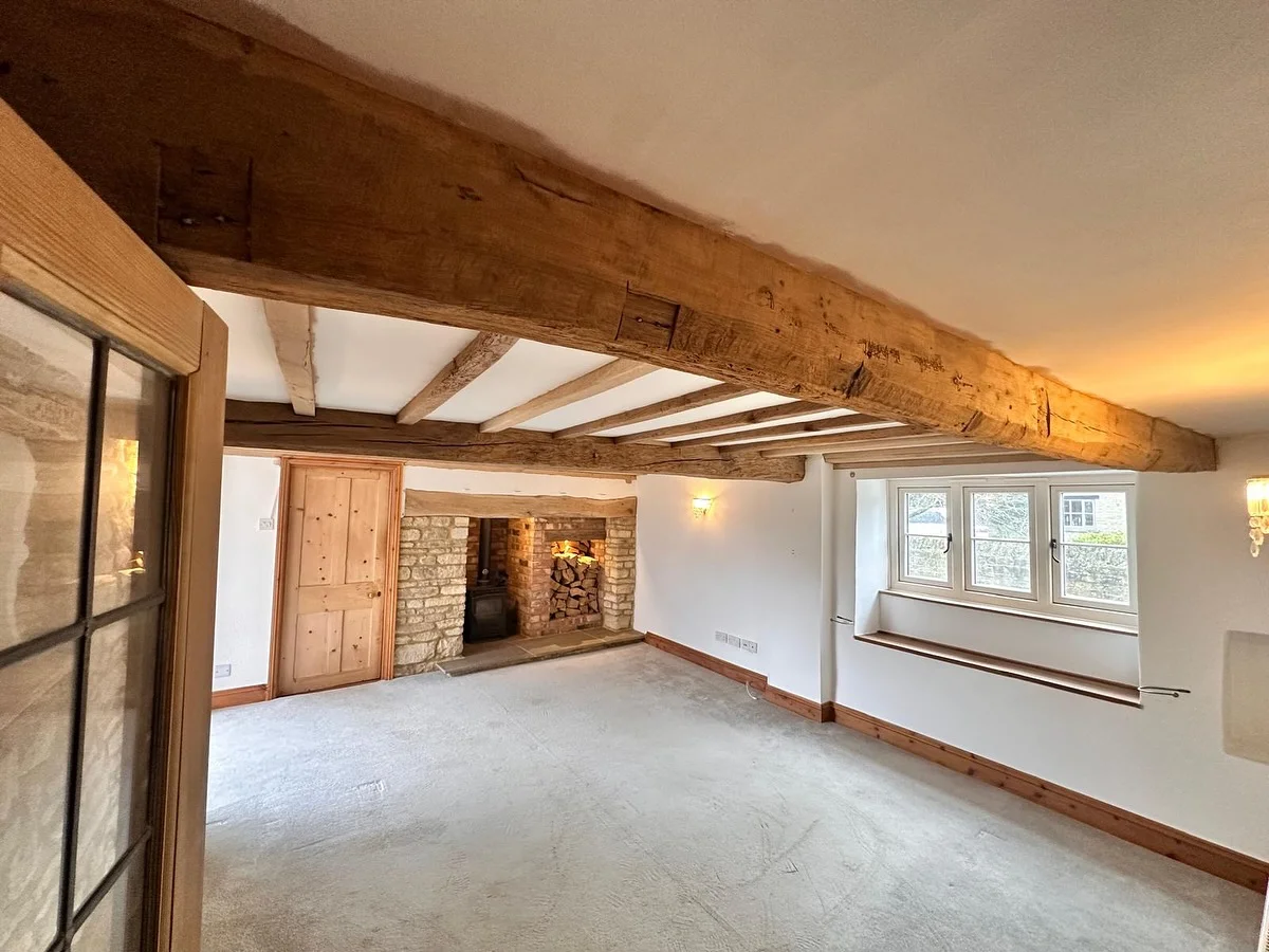 Sandblasted oak beams above a restored stone fireplace in a bright character interior